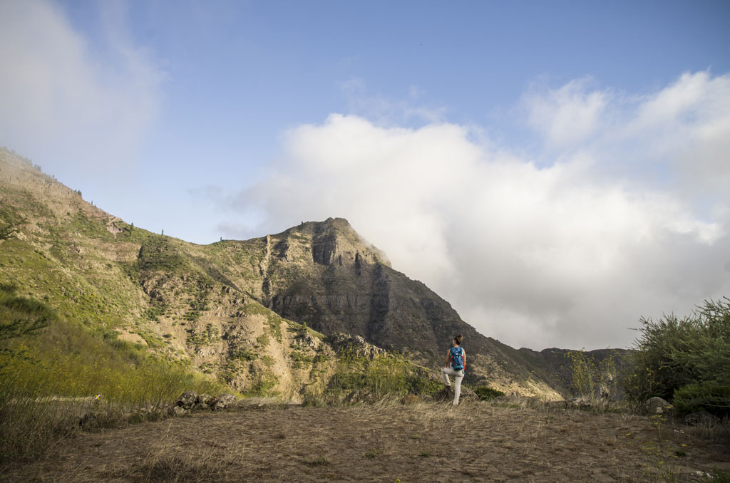 Persona caminando frente a montañas en Tenerife bajo un cielo parcialmente nublado.
