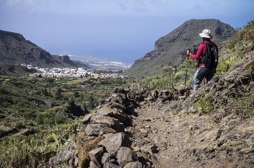 Senderista con bastones en un sendero montañoso, vista de Masca, Tenerife.