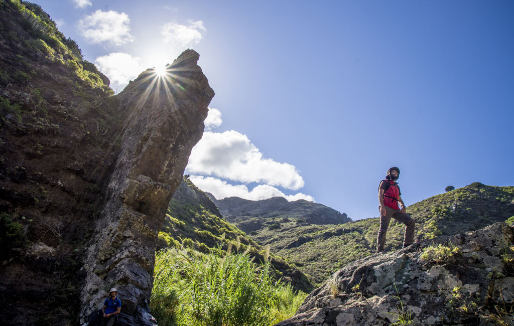 Persona haciendo senderismo en el barranco de Masca, Tenerife, con el sol brillando detrás.