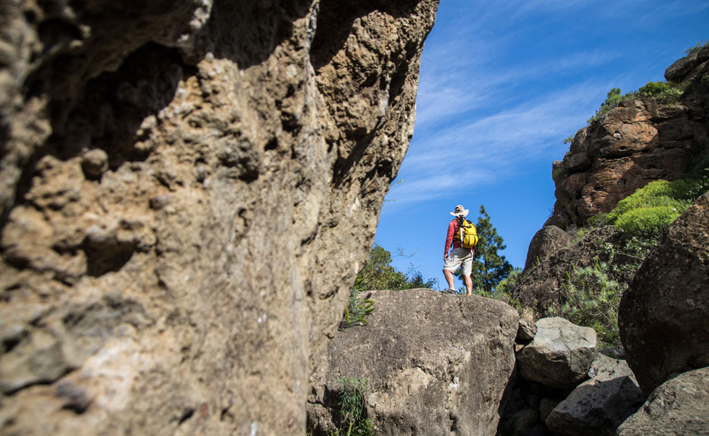 Persona con mochila amarilla en sendero rocoso en Tenerife bajo cielo azul.
