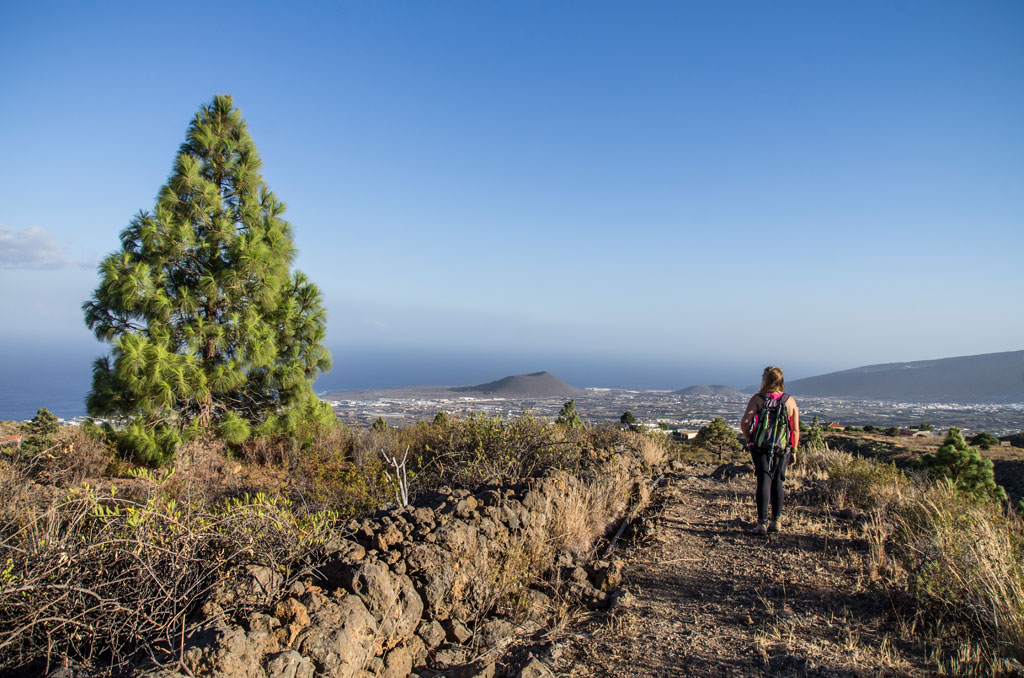 Persona caminando por sendero en Las Cañadas del Teide, Tenerife, con vista al mar.