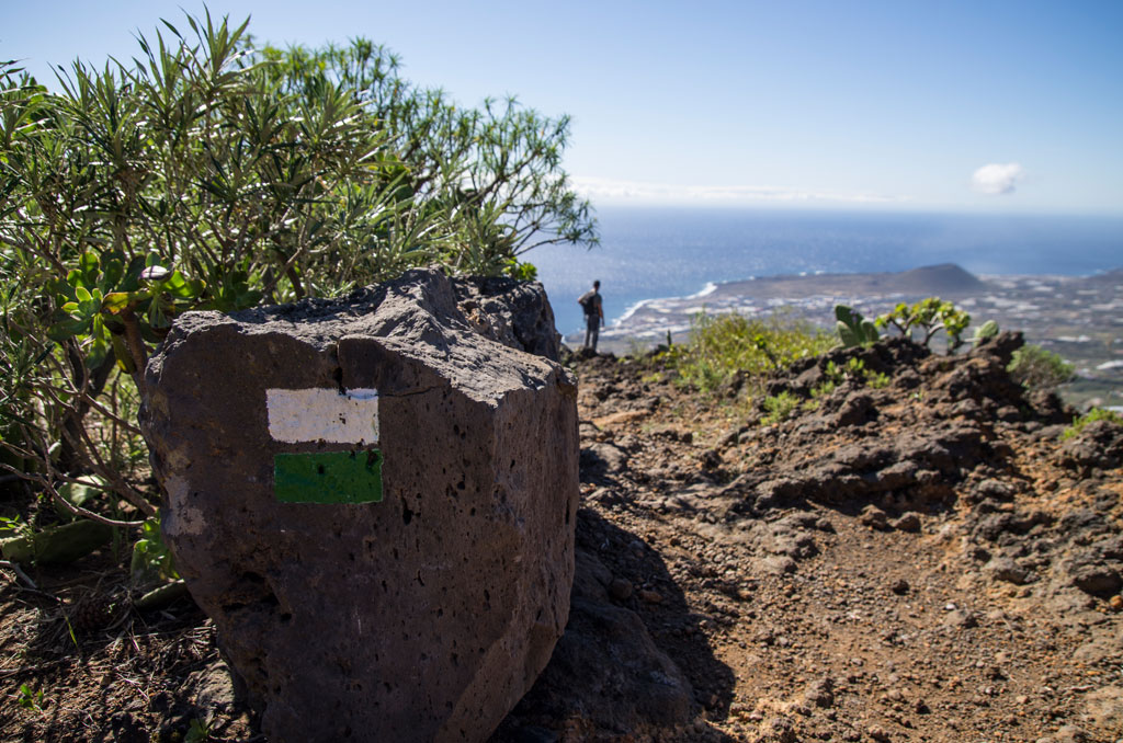 Sendero en Tenerife con roca marcada y vistas al mar.