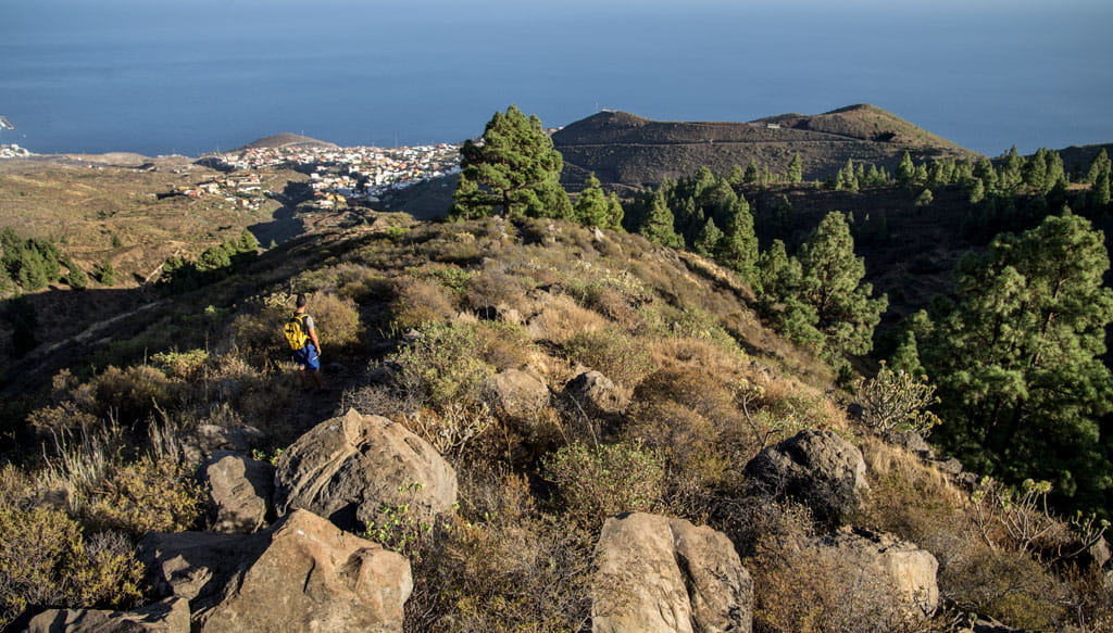 Sendero montañoso en Tenerife con vistas al mar y un caminante con mochila.