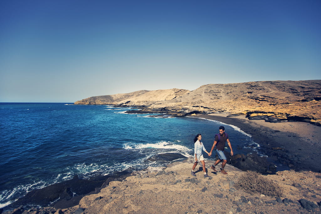Pareja caminando junto al mar en un paisaje costero de Tenerife.