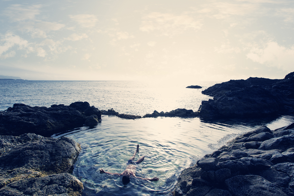 Persona flotando en una piscina natural rodeada de rocas junto al océano en Tenerife.