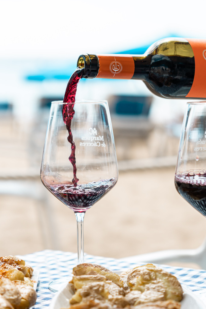 Vino tinto vertido en copa junto a pasteles en mesa de playa en Tenerife.