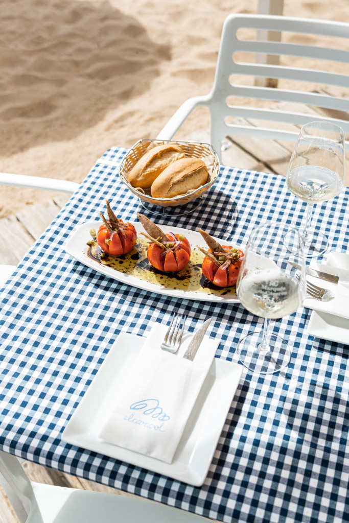 Mesa con tomates rellenos, pan y copa de vino en frente de la playa El Ancla en Tenerife.