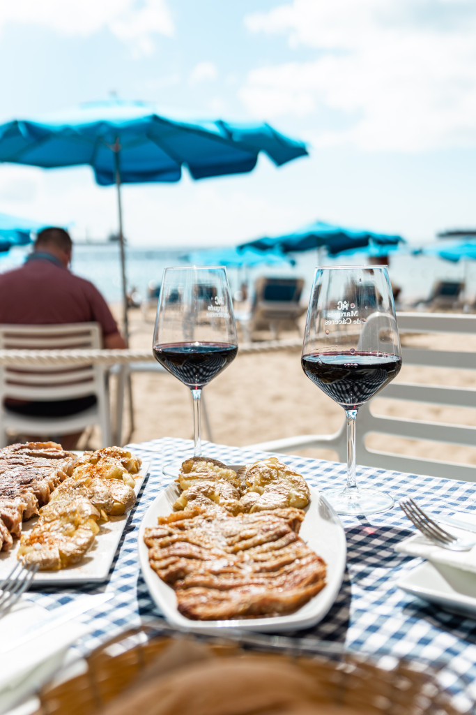 Vasos de vino y comida en la playa con sombrillas azules en Tenerife.