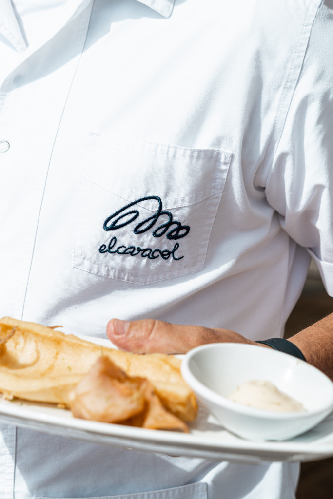 Camarero con camisa blanca de el caracol llevando plato de comida.
