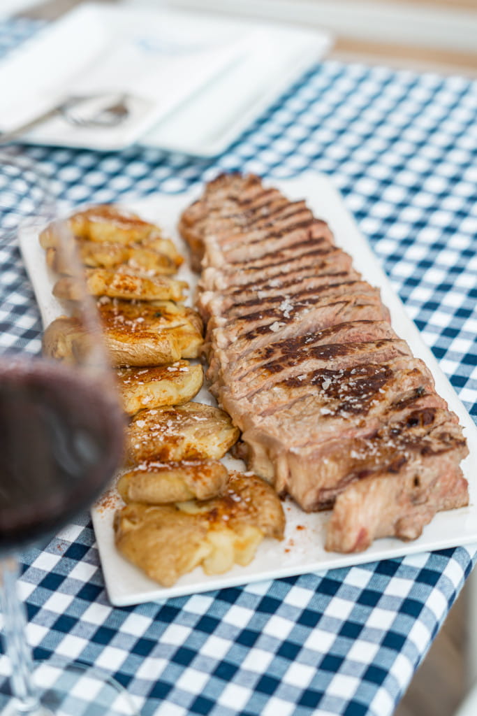 Carne a la parrilla con papas en plato sobre mantel de cuadros en Tenerife.