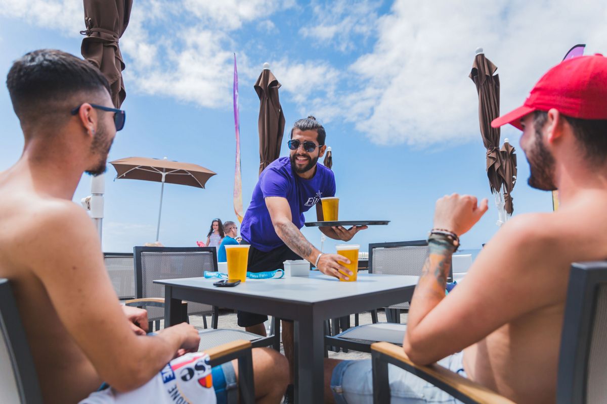 Camarero sirviendo cervezas a dos hombres en una terraza en Tenerife.