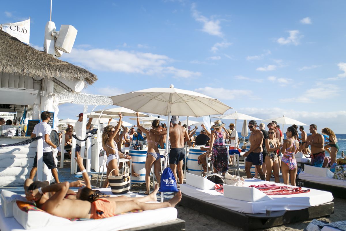 Personas disfrutando en un club de playa en Tenerife bajo sombrillas.
