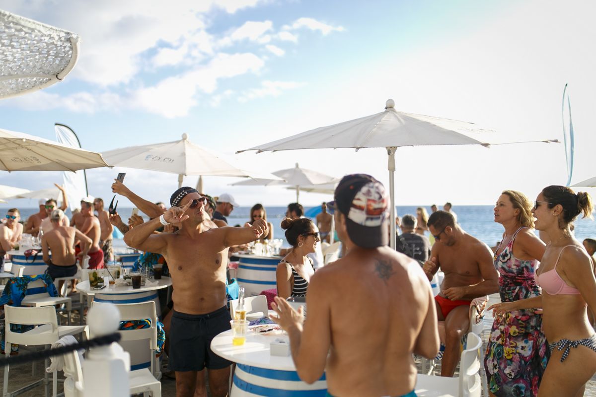 Personas disfrutando de una fiesta en la playa en Tenerife, con sombrillas y mesas.