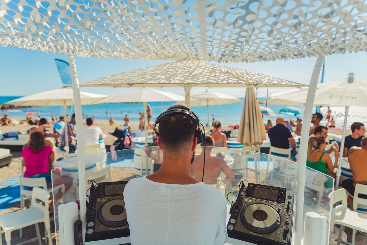 DJ tocando música en una playa de Tenerife con personas disfrutando del mar.