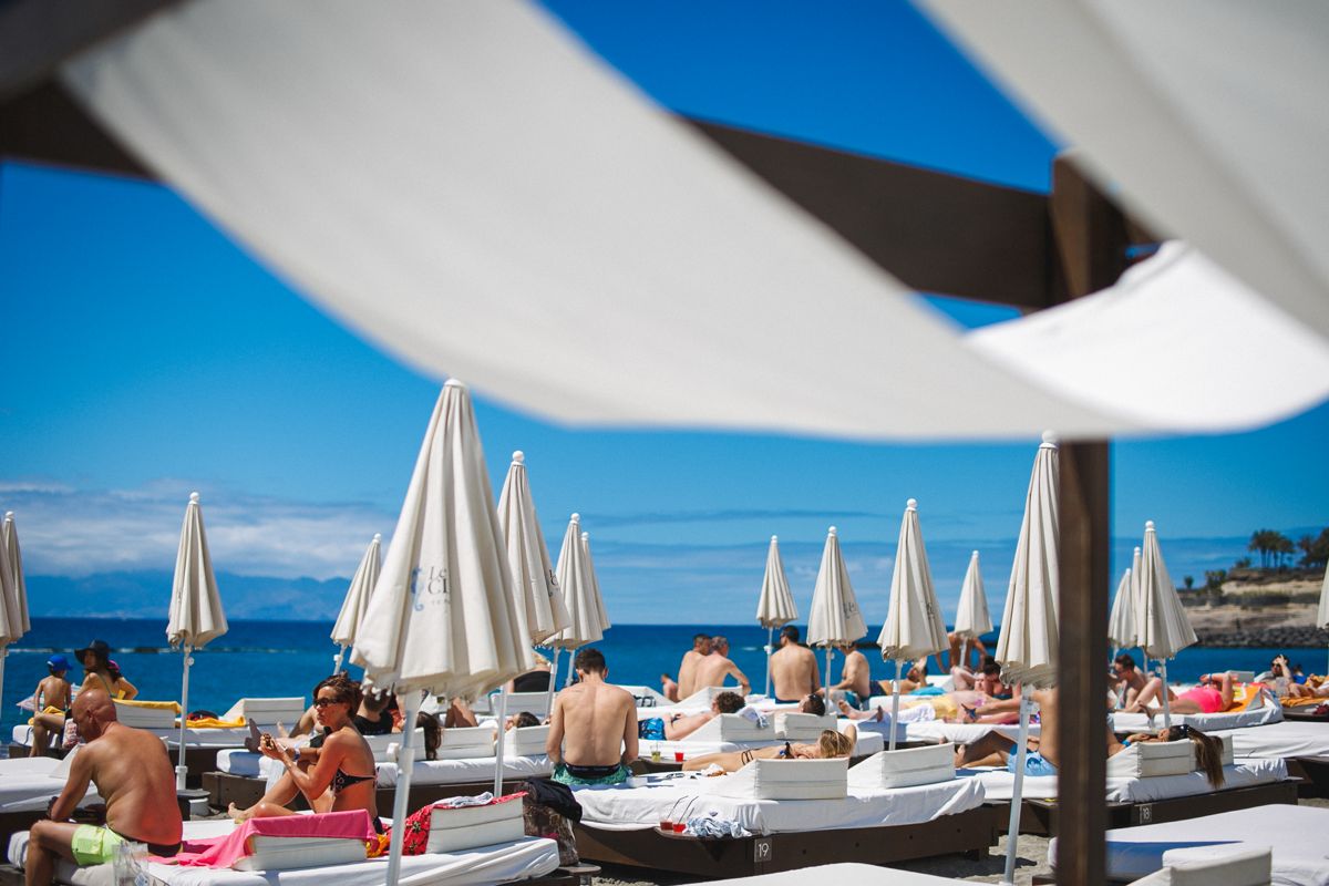 Personas tomando el sol en hamacas bajo sombrillas en playa de Tenerife.