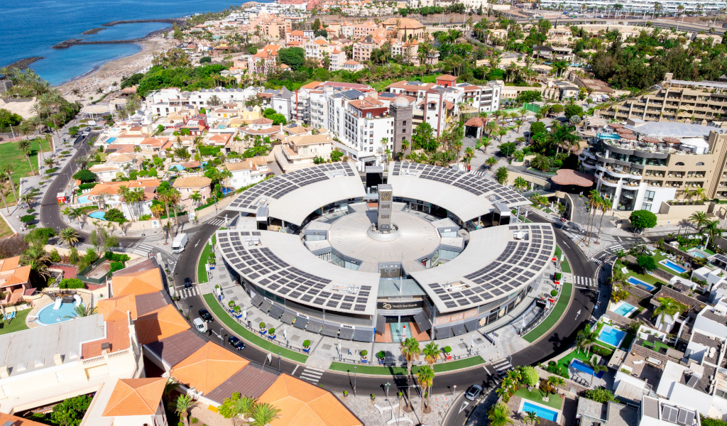 Vista aérea del centro comercial Plaza del Duque en Tenerife, rodeado de edificios y el mar.