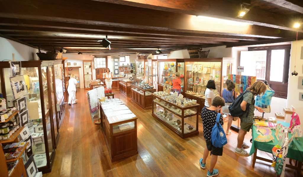 Visitantes en una tienda de artesanías en Tenerife, observando productos en vitrinas de madera.