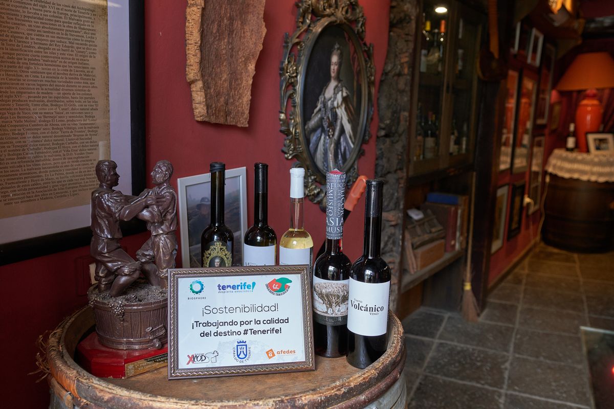 Botellas de vino y cartel de sostenibilidad sobre barril en establecimiento de Tenerife.