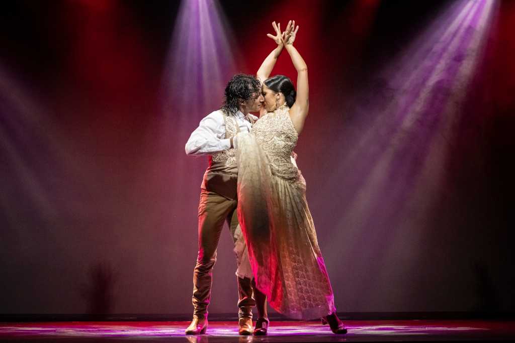 Pareja bailando flamenco bajo luces brillantes en un escenario.