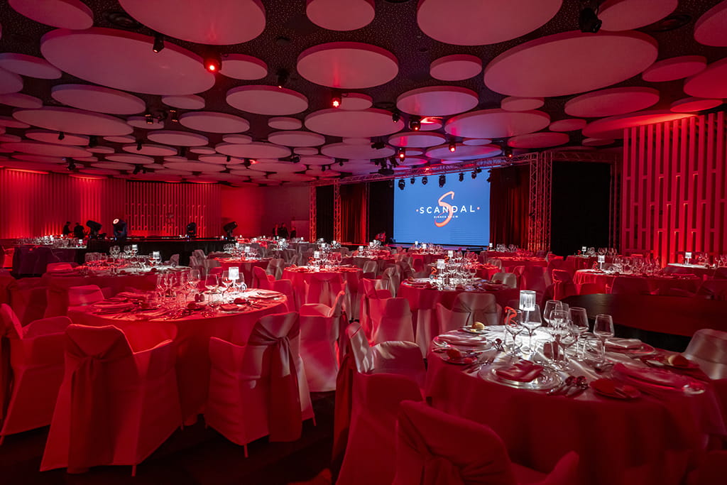 Salón de eventos con mesas decoradas y pantalla con logo SCANDAL Show Tenerife.