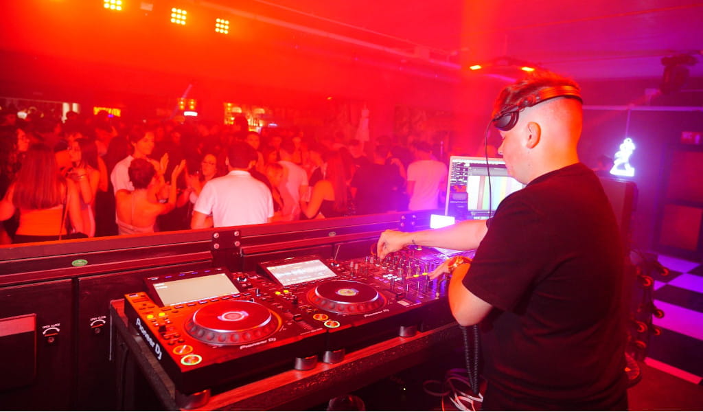 DJ animando fiesta en club nocturno en Tenerife con luces rojas y público bailando.