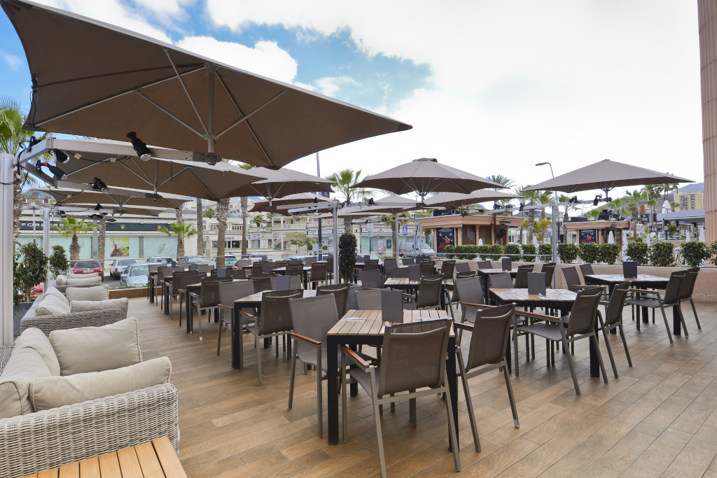 Terraza con mesas y sillas bajo sombrillas en centro comercial de Tenerife.
