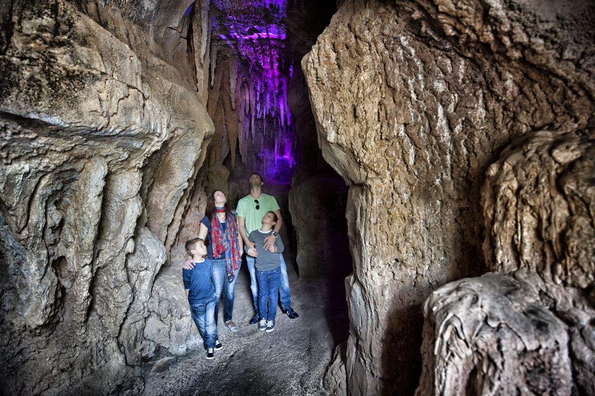Familia explorando una cueva en Tenerife, iluminación morada destacando el interior.