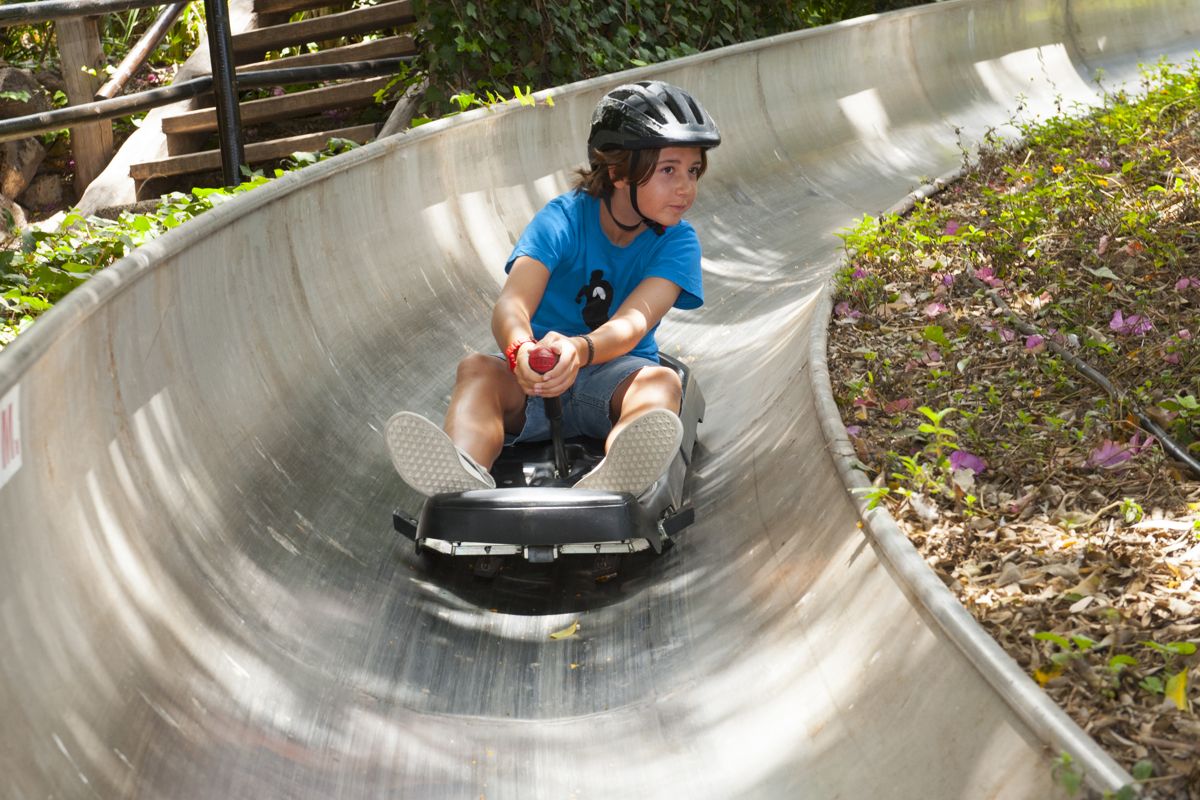 Niño con casco negro deslizando en tobogán de metal curvo en Tenerife.