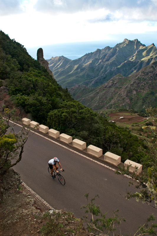 Ciclista en carretera de montaña en Anaga, Tenerife, con vistas al mar y montañas.