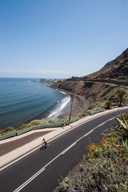 Ciclista en carretera costera de Tenerife con vista al mar y acantilados.