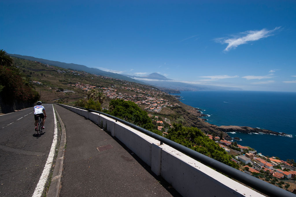 Ciclista recorriendo carretera con vistas al Teide y costa en Tenerife.