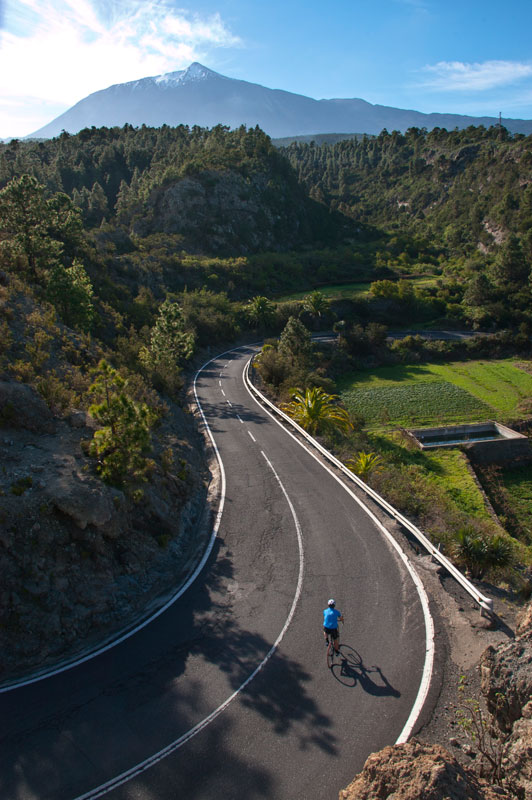 Ciclista en carretera rodeada de montañas y vegetación en Tenerife.
