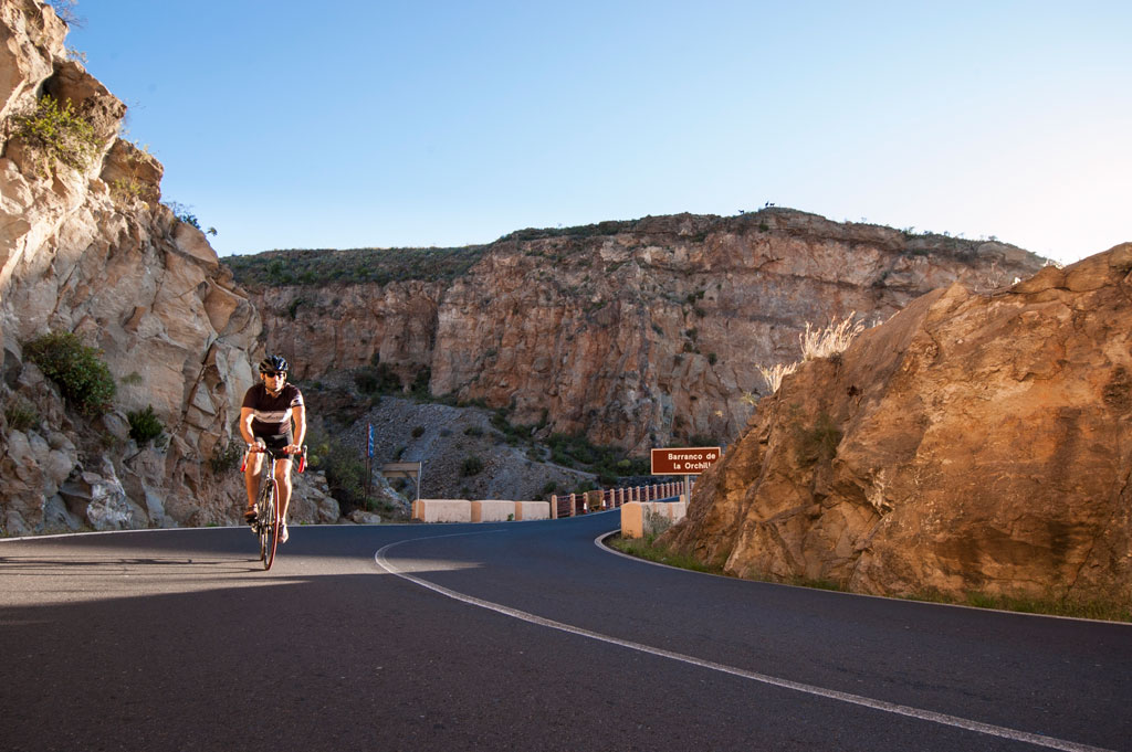 Ciclista en la carretera del Barranco de la Orchilla en Tenerife con paisaje rocoso.