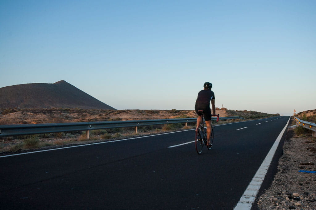Ciclista en carretera cerca de un volcán en Tenerife al atardecer.