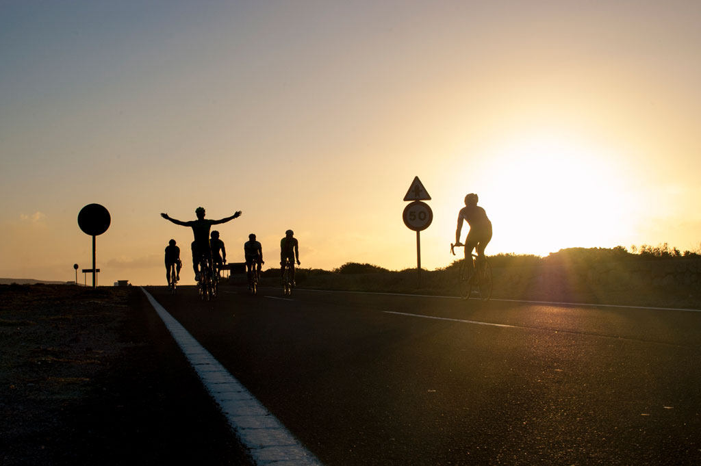 Ciclistas en carretera al atardecer en Tenerife, junto a señal de velocidad 50.