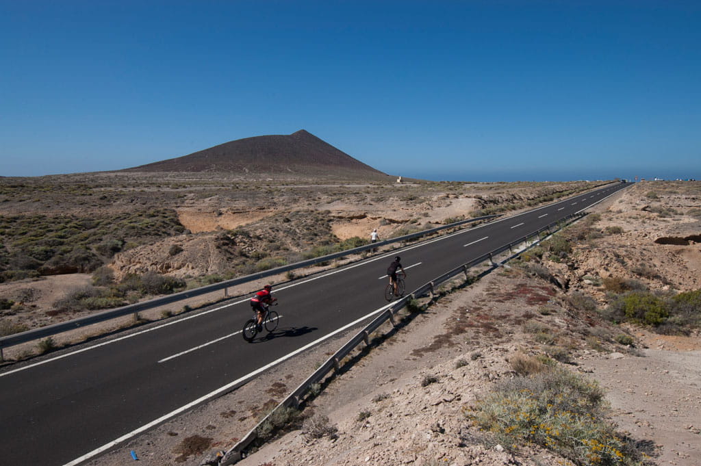 Ciclistas en carretera hacia montaña en Tenerife bajo el cielo despejado.