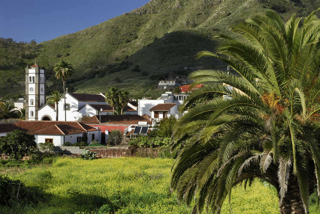 Paisaje de Taganana en Tenerife con iglesia y palmeras verdes delante de montañas.