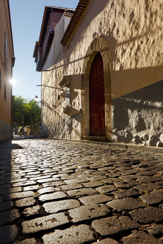 Calle adoquinada con puerta de arco y luz solar en La Laguna, Tenerife.