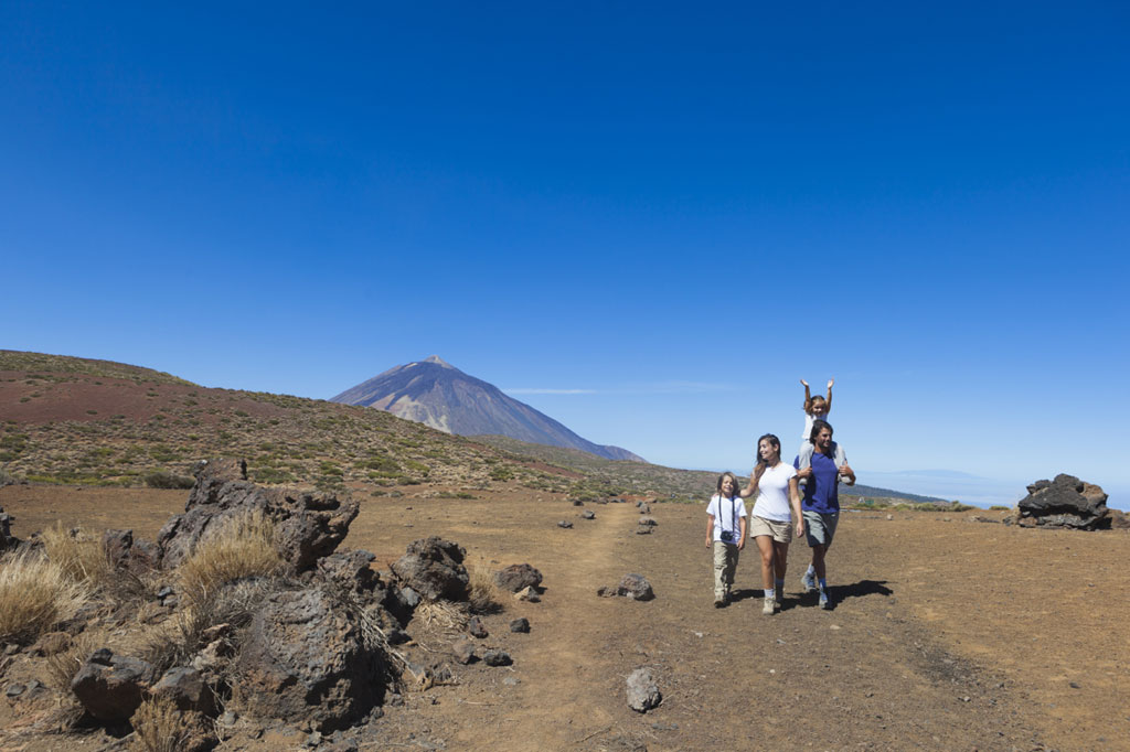 Familia caminando por sendero en el Teide, Tenerife, con el volcán al fondo.