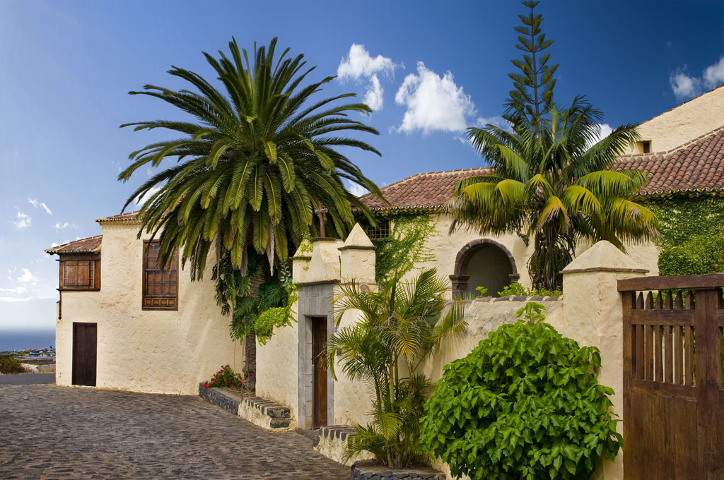 Casa histórica con palmeras en La Orotava, Tenerife. Cielo despejado y muro de piedra.