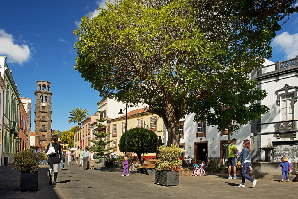 Personas caminando en la plaza con torre de iglesia en La Laguna, Tenerife.