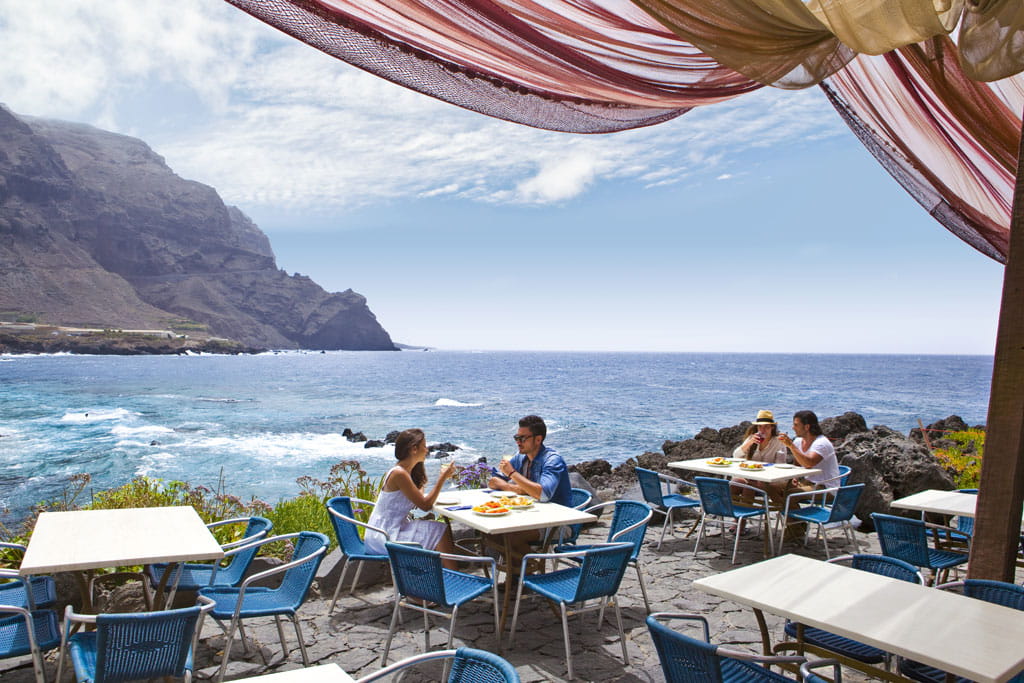 Terraza frente al mar en Tenerife con personas comiendo bajo un cielo despejado.