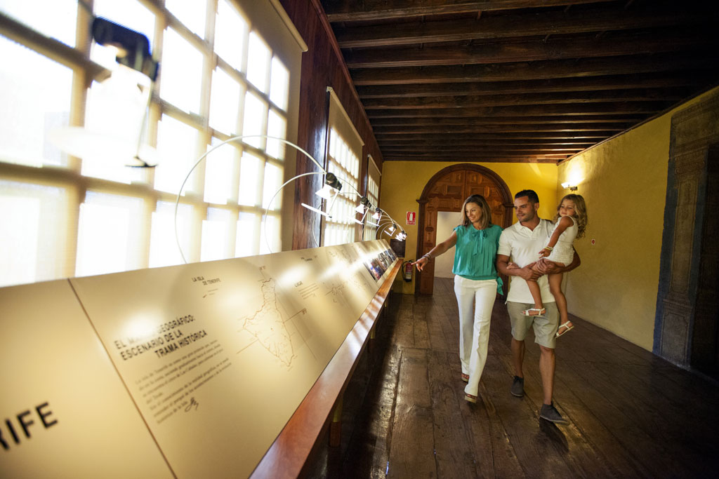 Familia recorriendo un museo en Tenerife, observando exhibición iluminada en pasillo de madera.