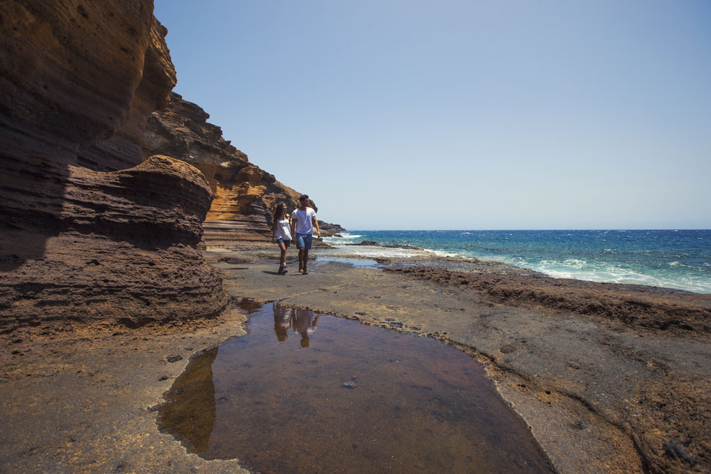 Personas caminando en la costa rocosa de Tenerife junto al mar.