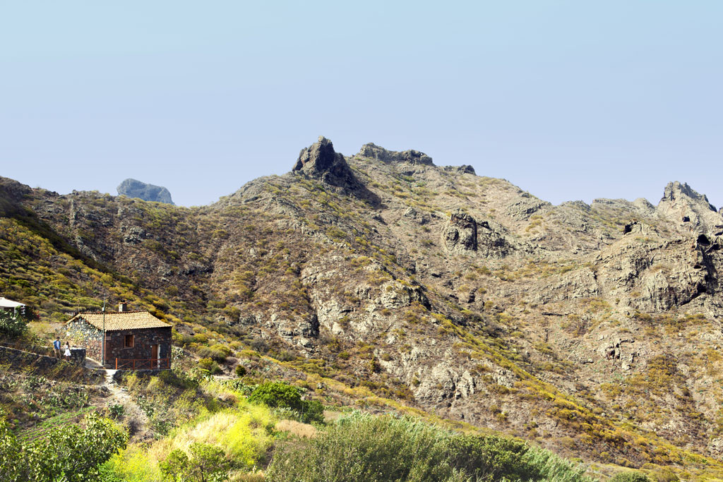 Casa de piedra en paisaje montañoso de Masca, Tenerife, con vegetación alrededor.