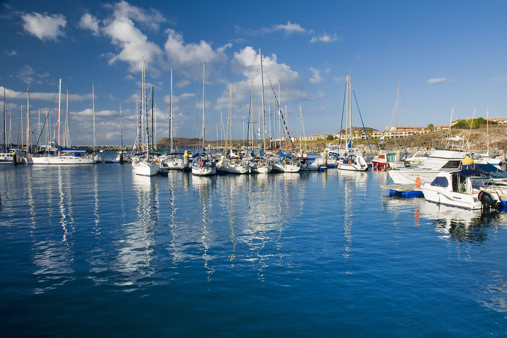 Barcos anclados en el puerto de Las Galletas, Tenerife, bajo un cielo azul.