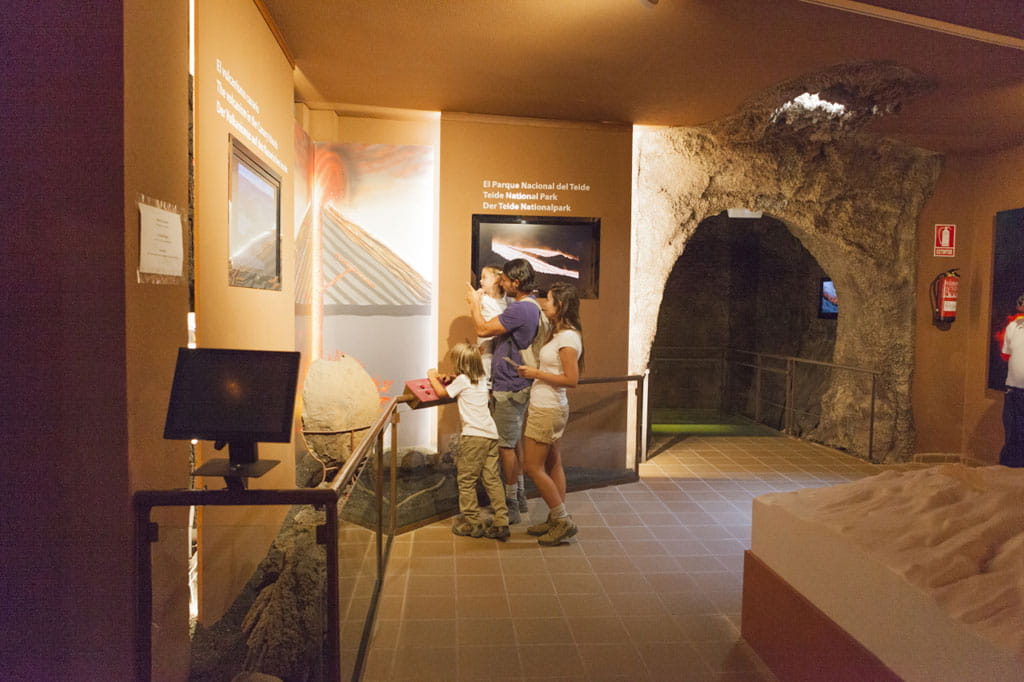 Visitantes observan exposición del Parque Nacional del Teide en interior de cueva simulada.