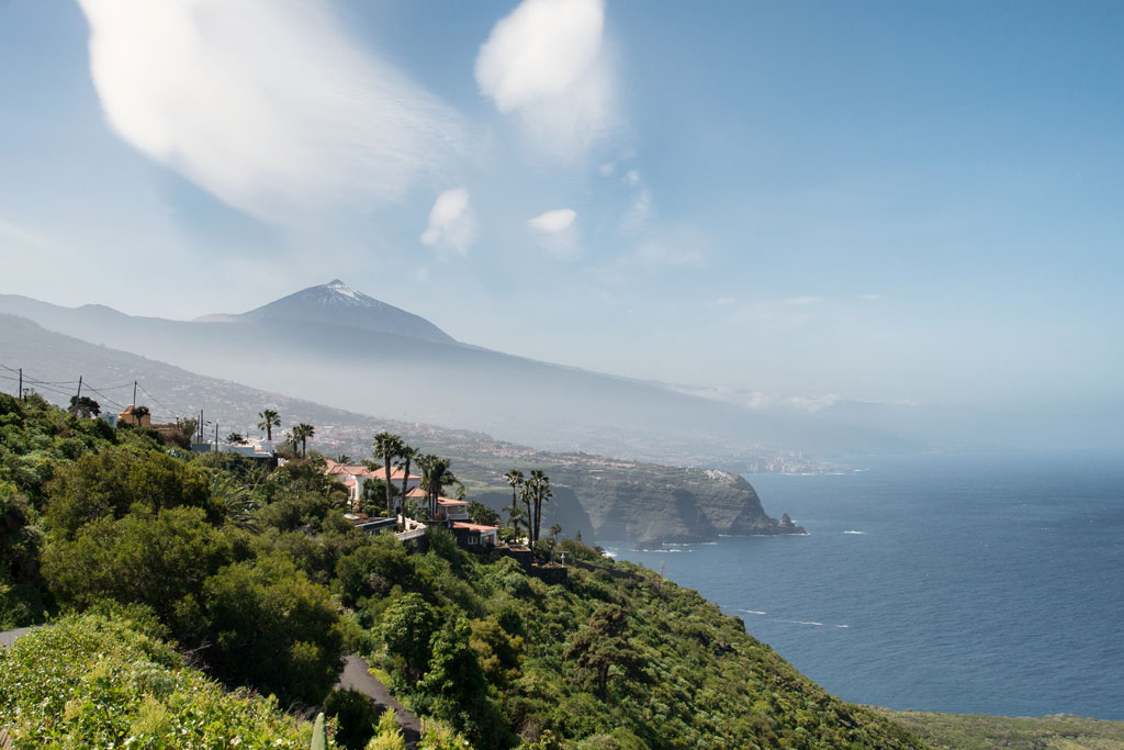 Vista del Teide desde la costa de Tenerife, con mar y vegetación en primer plano.