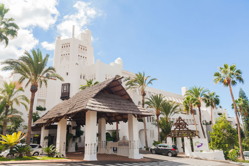 Entrada principal de hotel con arquitectura blanca y palmeras en Tenerife.