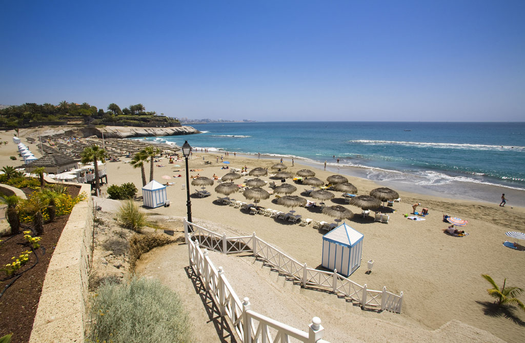 Playa del Duque en Tenerife con sombrillas y bañistas disfrutando del sol.